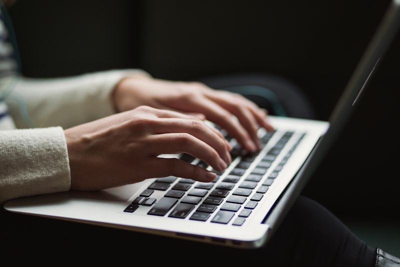 Hands typing on a sleek laptop keyboard in a dark, modern workspace